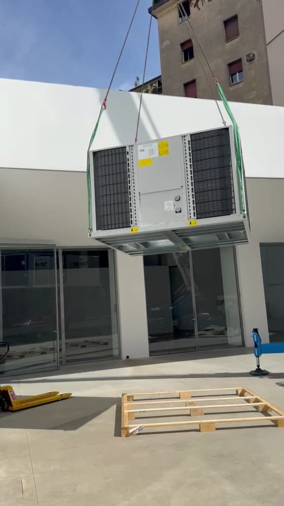 Unità esterna di climatizzazione sollevata con gru davanti alla facciata di un edificio